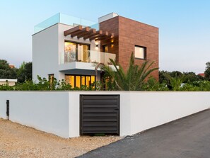 A modern two-story house with a flat roof, large windows, and a wooden facade. - Beautiful villa Tamaria with heated pool by Interhome (Nin)