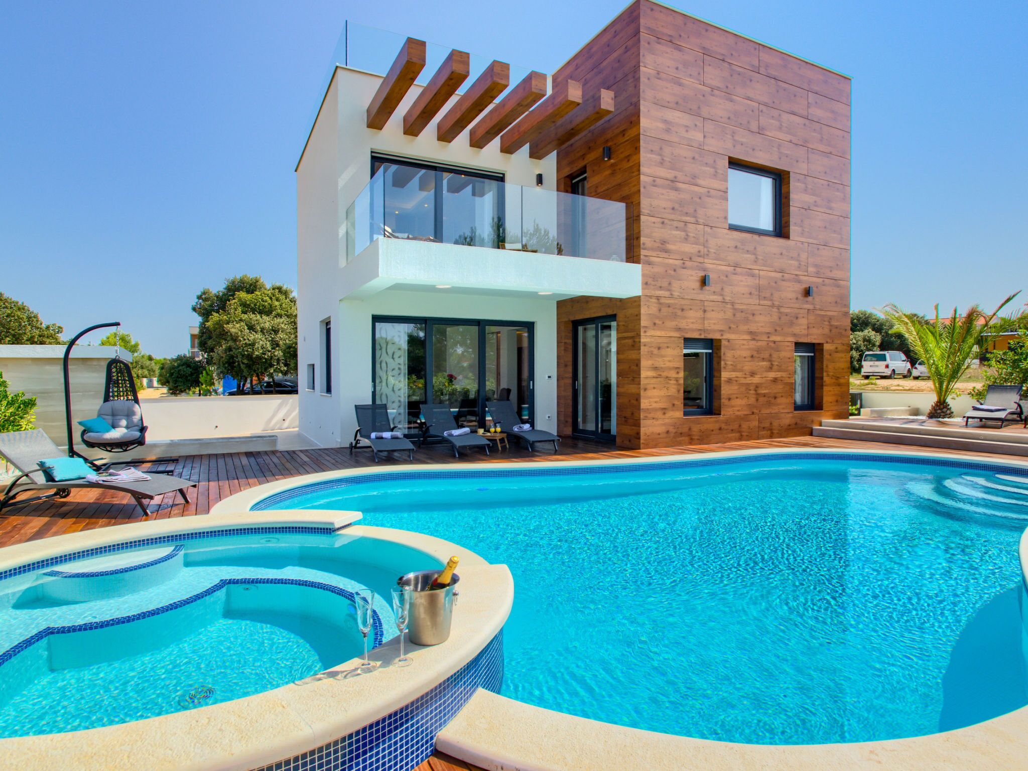 A modern two-story house with a swimming pool, lounge chairs, and a hot tub.
