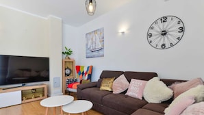 A modern living room with a flat-screen TV, a large wall clock, and a sofa with decorative pillows. - Vacation home  by Interhome (Nin)