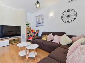 Ein modernes Wohnzimmer mit Flachbildfernseher, einer großen Wanduhr und einem Sofa mit Zierkissen.