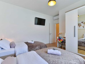 A hotel room with two beds, a flat-screen TV mounted on the wall, a desk with a chair, and a wardrobe. - Villa First Hill with heated pool by Interhome (Nin)