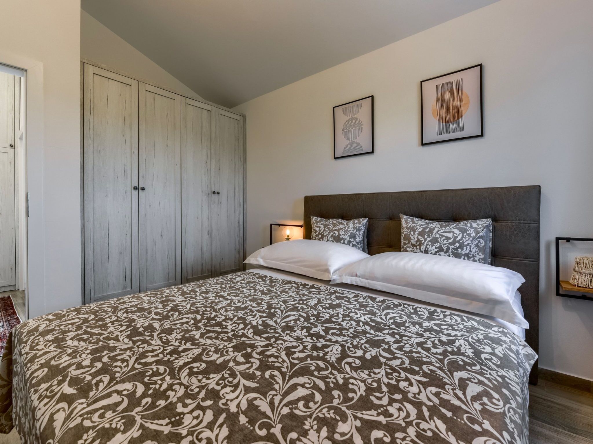 Ein Schlafzimmer mit einem großen Bett, einem Kleiderschrank und zwei gerahmten Kunstwerken an der Wand.