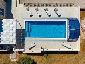 Ein rechteckiger Swimmingpool mit Glasveranda, umgeben von Liegestühlen und einer überdachten Sitzgruppe.