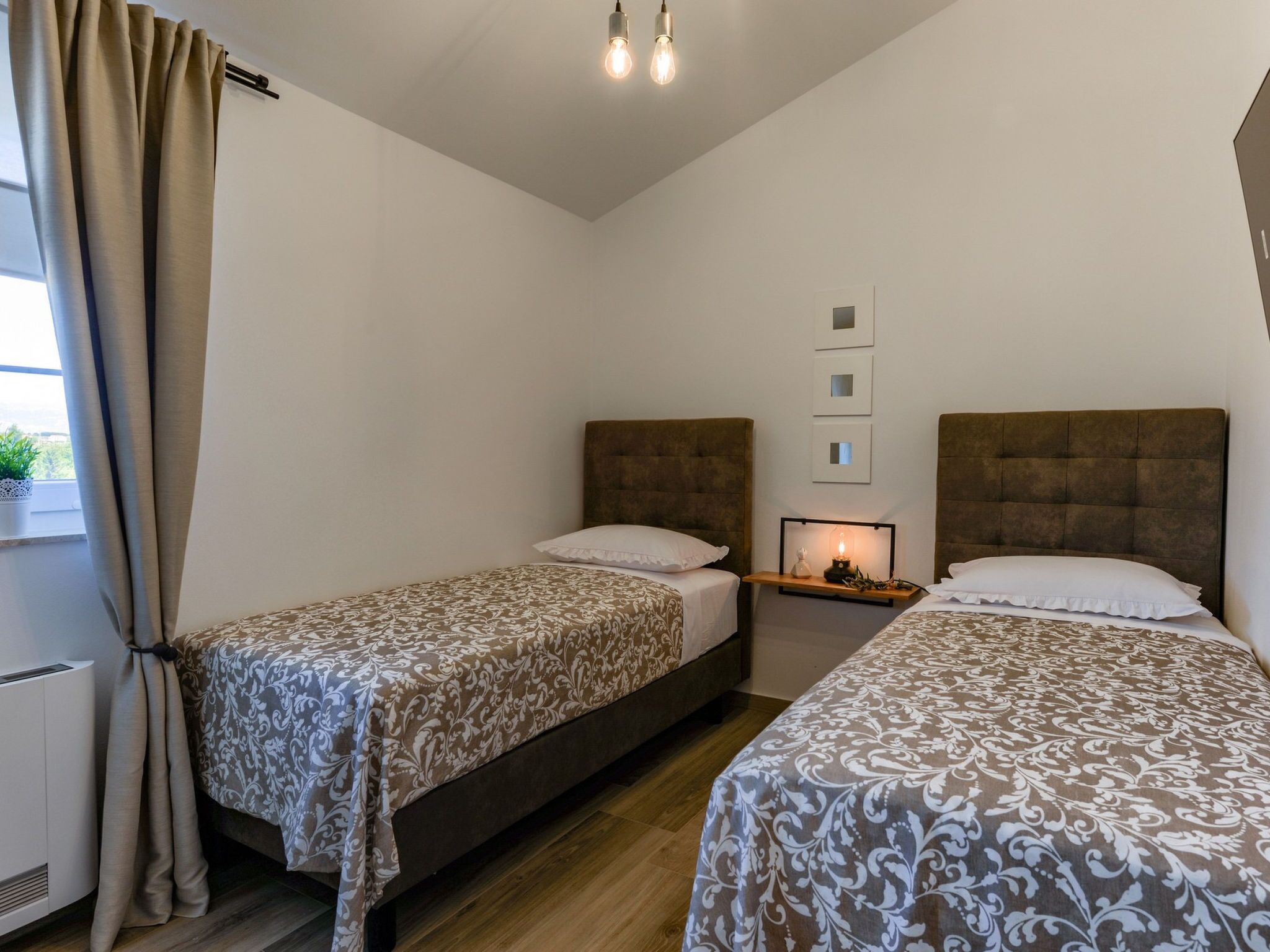 Une chambre d’hôtel avec deux lits, une table de chevet avec une lampe et une fenêtre avec des rideaux.