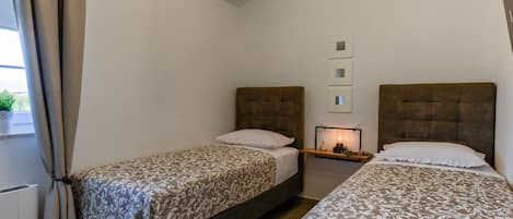 Une chambre d’hôtel avec deux lits, une table de chevet avec une lampe et une fenêtre avec des rideaux.