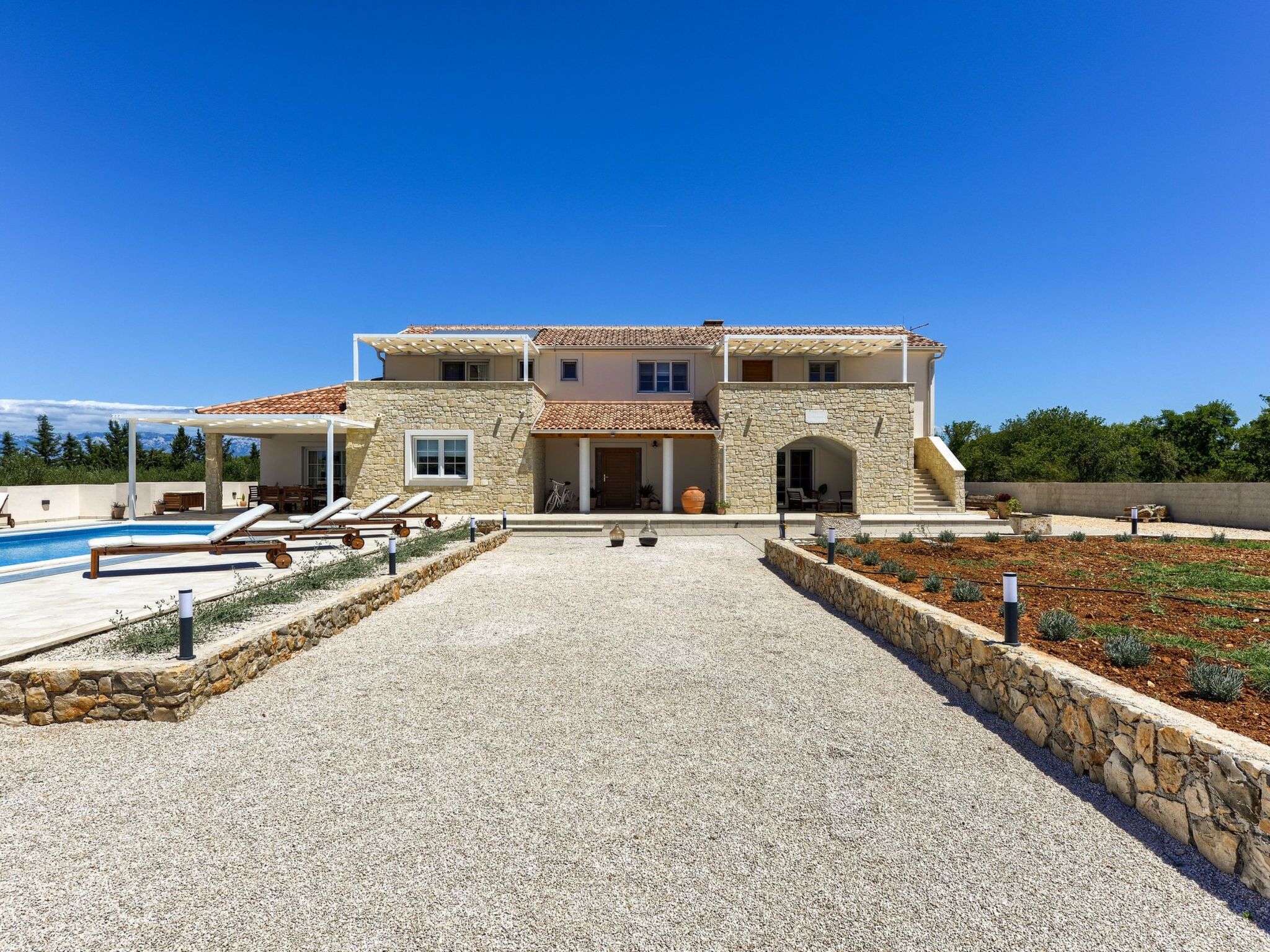 A two-story house with a stone facade, a swimming pool, and a well-maintained garden.