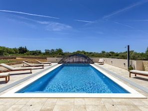 Ein rechteckiger Swimmingpool mit glasklarer blauer Wasseroberfläche, umgeben von einer gefliesten Liegefläche.