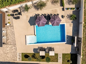 An aerial view of a swimming pool area with sun loungers, umbrellas, and a small garden. - Villa Miranda with pool by Interhome (Nin)