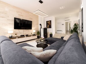 A modern living room with a large flat-screen TV, grey sofas, a coffee table, and a wooden accent wall. - Villa Miranda with pool by Interhome (Nin)