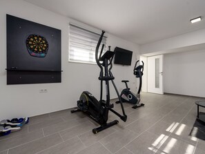 Ein Heimfitnessraum mit Trainingsgeräten, einer Dartscheibe und einem Fernseher an der Wand.
