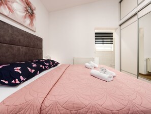 Ein Schlafzimmer mit Bett, Kissen, Heizkörper und einem Fenster mit Jalousien.