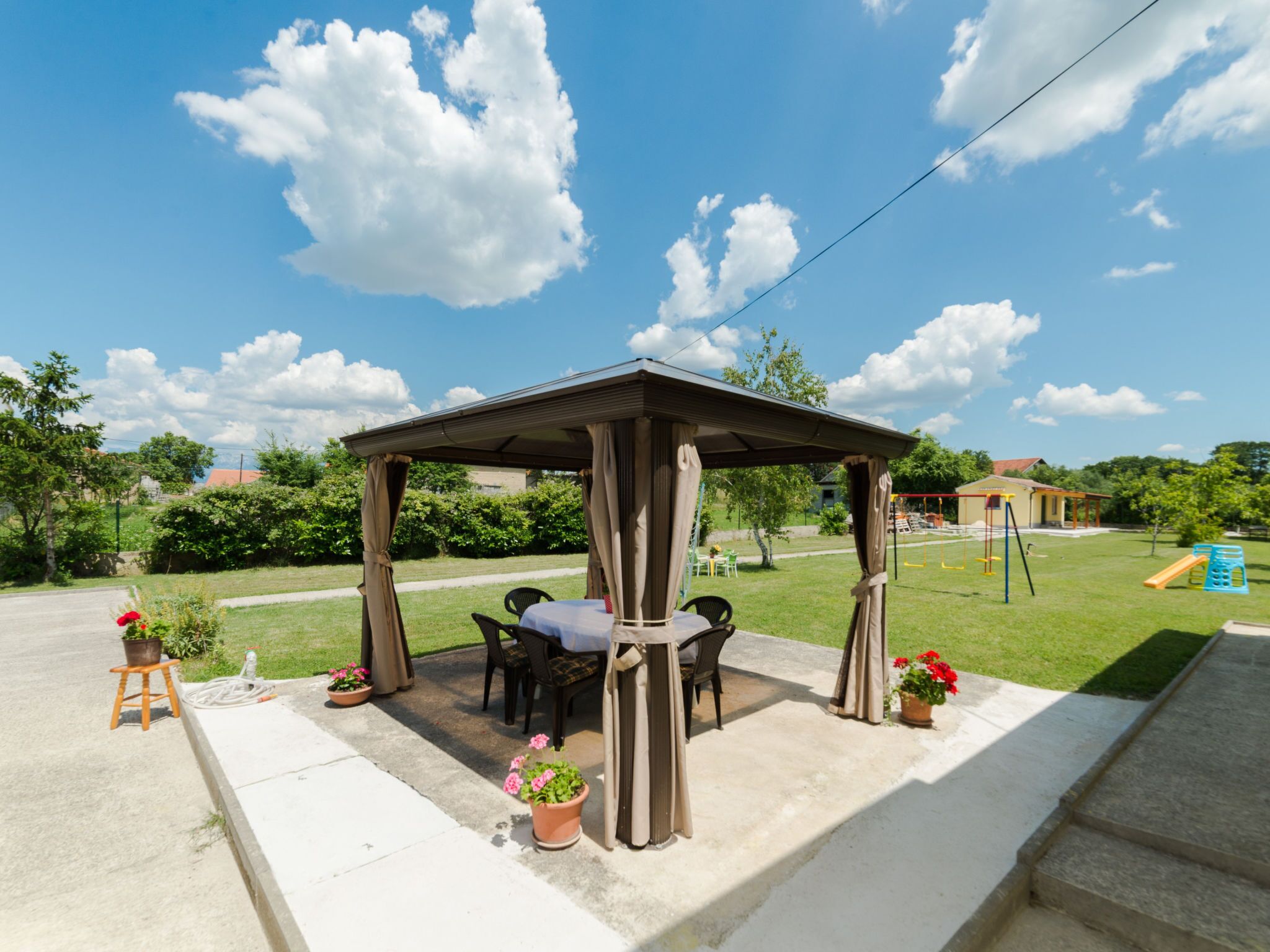 Un espace extérieur abrité, avec une table et des chaises, entouré de plantes en pot et sous un ciel dégagé.