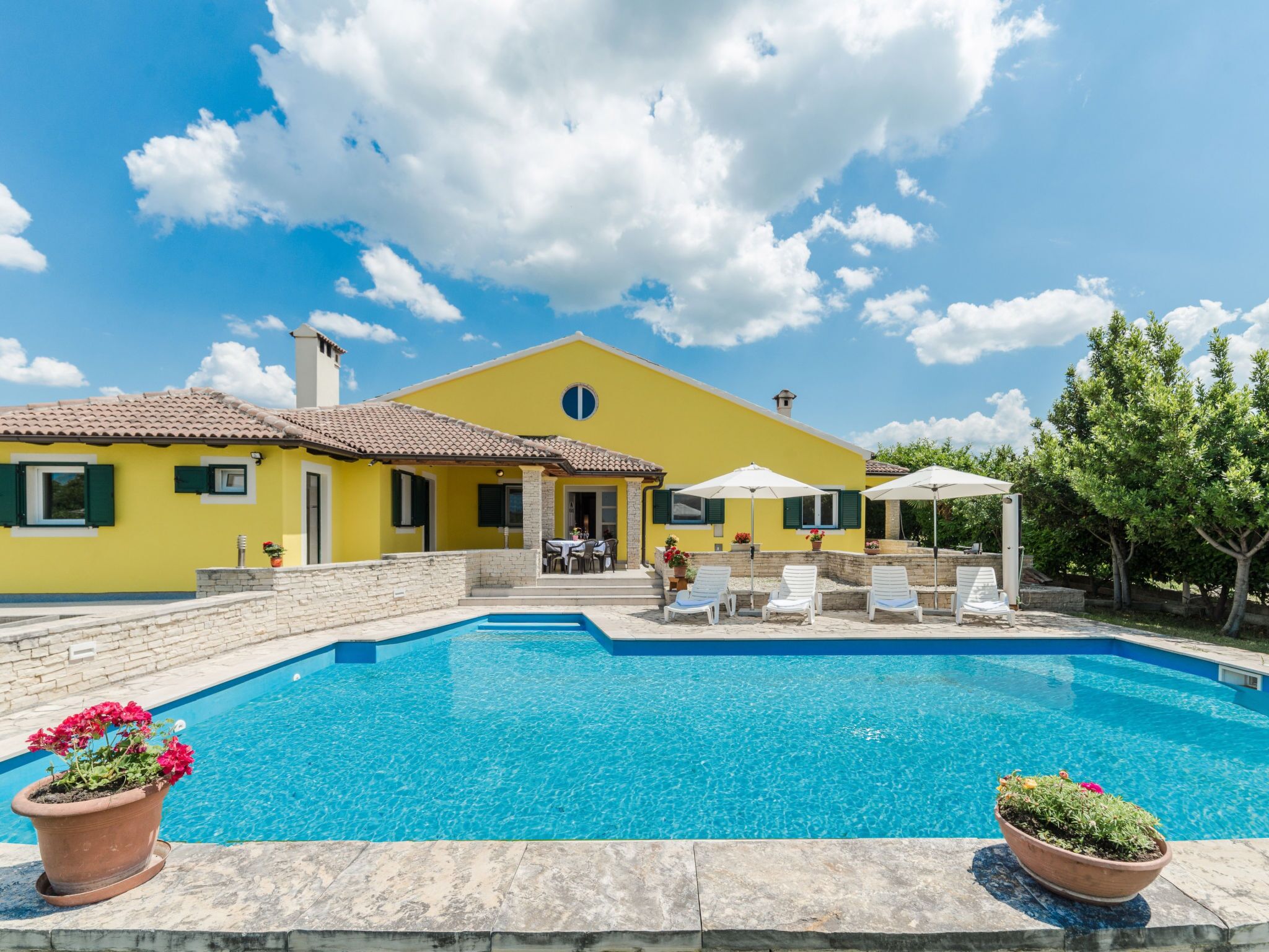 A yellow villa with a swimming pool, outdoor seating, and a garden.
