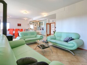A living room with a green sofa, a coffee table, and a dining area with red chairs. - Villa Ana with large pool by Interhome (Policnik)