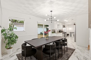 A modern kitchen with white cabinets, a marble floor, and a dining area with a dark table and chairs. - World Cup Villa · 7-Min Walk to AT&T Stadium (Arlington)
