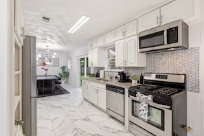 A modern kitchen with white cabinets, a stainless steel stove, a microwave, and a dishwasher. - World Cup Villa · 7-Min Walk to AT&T Stadium (Arlington)