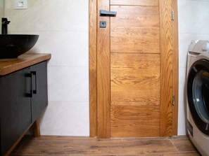 Eine Holztür mit Schlüsselloch, eine Waschmaschine und ein dunkel gefärbtes Schranksystem mit Waschbecken.