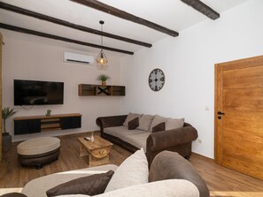 A living room with a sofa, coffee table, TV, and a wooden door. - Zen Garden Villa with heated pool by Interhome (Posedarje)