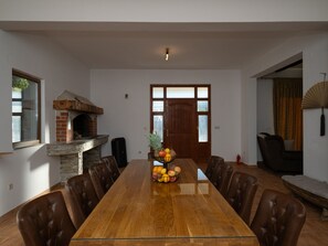 A spacious dining room with a long wooden table, leather chairs, a brick fireplace, and a door with frosted glass panels. - Zen Garden Villa with heated pool by Interhome (Posedarje)