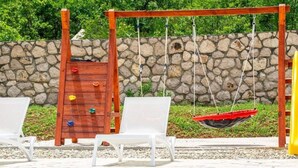 Uma área de piscina com um balanço de madeira, duas espreguiçadeiras brancas e um muro de pedra ao fundo.