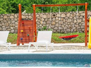 Ein Poolbereich mit einer Holzschaukel, zwei weißen Liegestühlen und einer Steinmauer im Hintergrund.