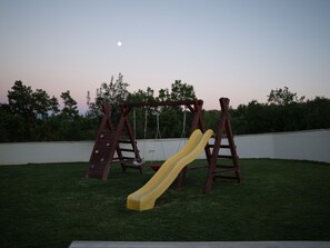 A wooden swing set with a yellow slide in a backyard. - Zen Garden Villa with heated pool by Interhome (Posedarje)
