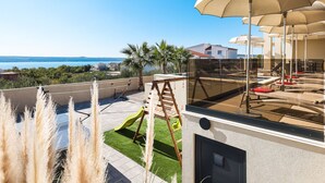 Een modern terras buiten met uitzicht op zee, een speelruimte voor kinderen en buitenzitplaatsen.