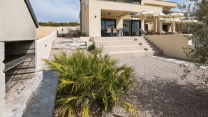 Een modern huis met twee verdiepingen en een patio met buitenmeubilair en parasols.