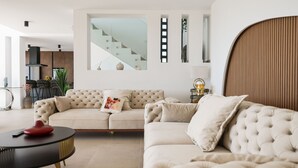 Een moderne woonkamer met een beige bank, een zwarte salontafel en een trap op de achtergrond.