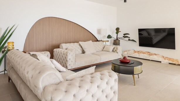 Een moderne woonkamer met een bank, een rond salontafeltje en een aan de muur bevestigde televisie.