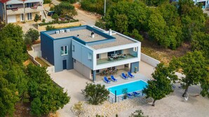 Ein modernes, zweistöckiges Haus mit Schwimmbad, Sitzgelegenheiten im Freien und einem Spielbereich.