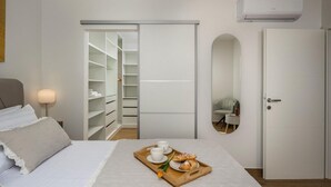 Ein Schlafzimmer mit Bett, Nachttisch mit Lampe, Schrank, Tür und einem Frühstücksbrettchen auf dem Bett.