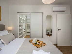 Quarto com cama, mesa de cabeceira com abajur, armário, porta e bandeja de café da manhã sobre a cama.