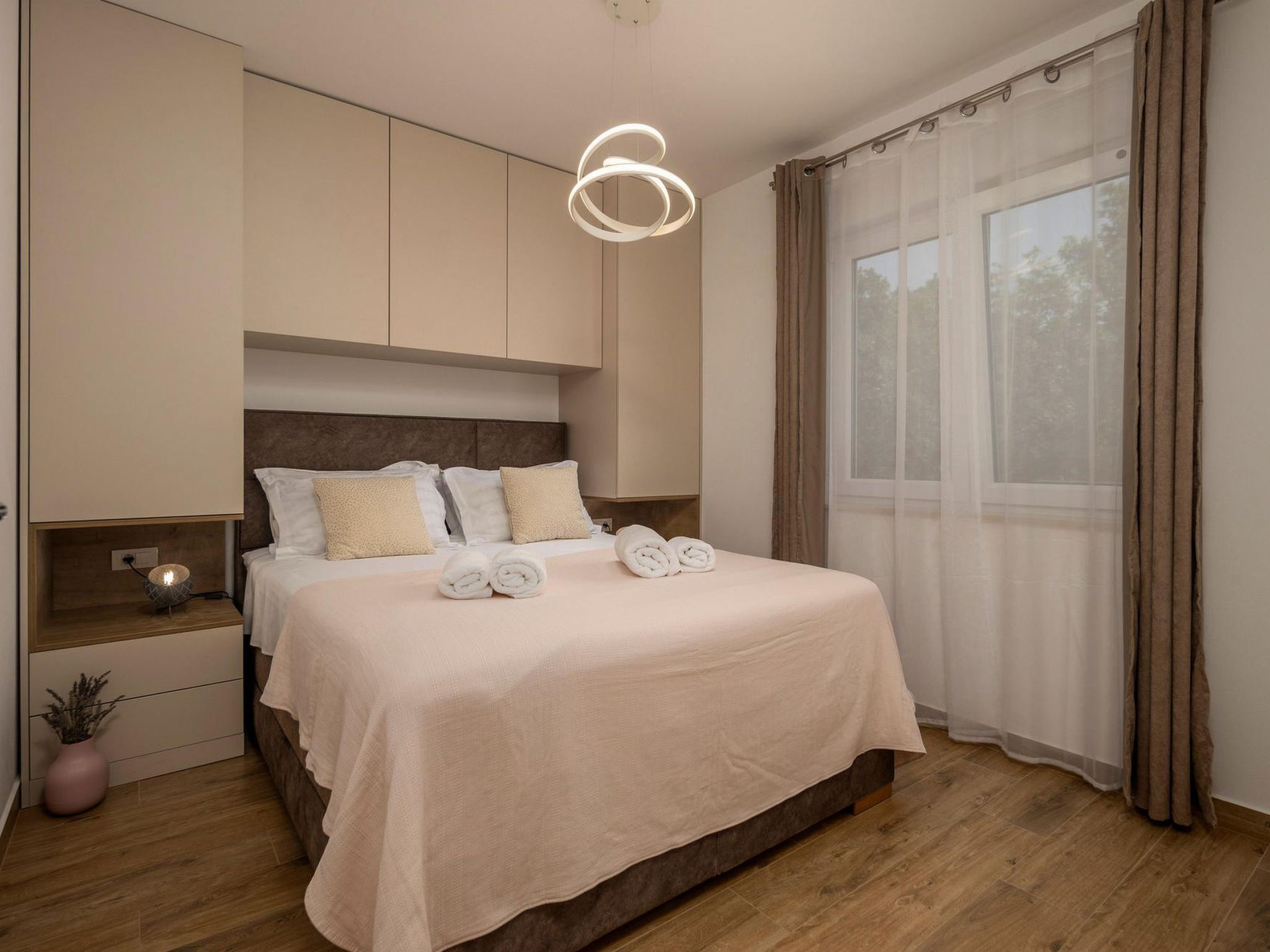 Un dormitorio moderno con una cama grande, una mesita de noche, una lámpara y una ventana con cortinas.