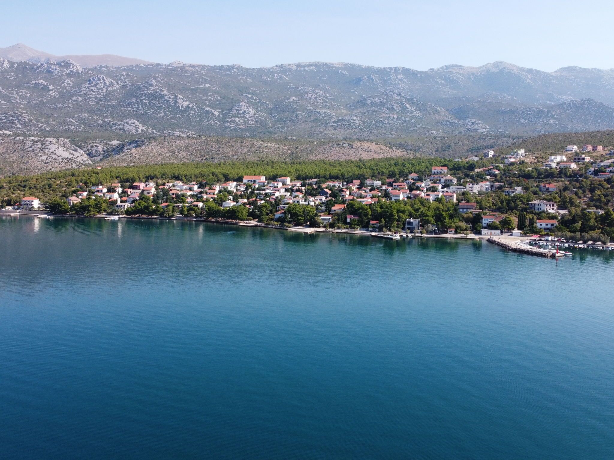 A coastal town with buildings along the shoreline, a pier, and mountains in the background.