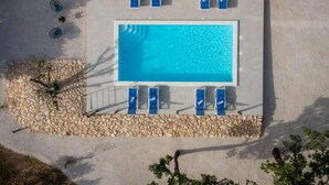 Ein rechteckiger Swimmingpool mit blauem Wasser, umgeben von einer Steinumrandung, und ausgestattet mit mehreren blauen Liegestühlen.