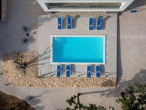 Piscina retangular com água azul, rodeada por uma borda de pedra e equipada com várias espreguiçadeiras azuis.