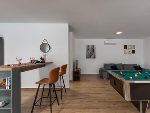 A modern living room with a pool table, a sofa, and a bar area with chairs. - Seaview Villa Deep Green with pool by Interhome (Rovanjska)