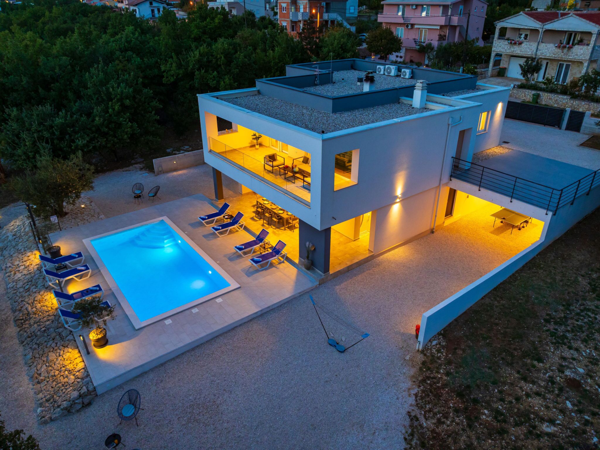 Ein modernes, zweistöckiges Haus mit Swimmingpool, Sitzgelegenheiten im Freien und einem Balkon.
