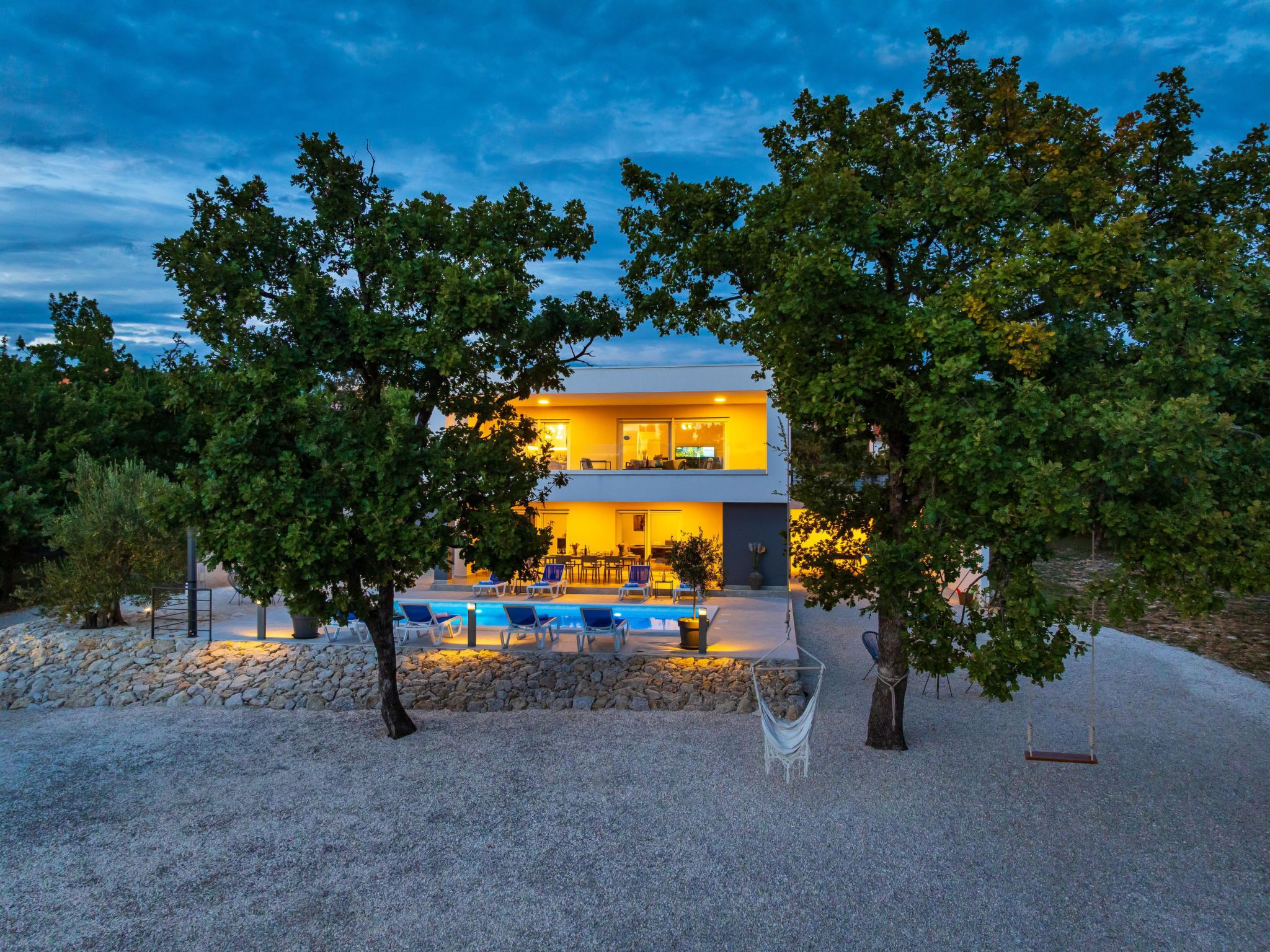 A modern two-story building with a swimming pool, outdoor seating, and trees.