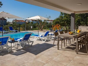 Ein Poolbereich mit Liegestühlen, Sonnenschirmen und einem Tisch mit Früchten und Getränken.