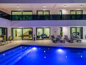 Ein modernes Wohngebäude mit zwei Etagen, einem Schwimmbad, Sitzgelegenheiten im Freien und einer Treppe, die zu einer oberen Ebene führt.