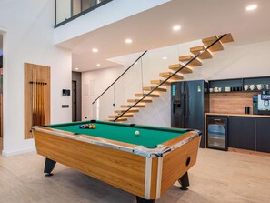 Uma mesa de bilhar em um ambiente moderno com escada e área de cozinha.