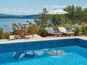 A poolside area with lounge chairs, a table with a wine glass, and an umbrella. - Beachfront villa Noa with heated pool by Interhome (Pridraga)