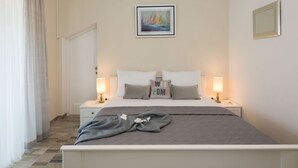 Une chambre d’hôtel avec un lit, deux tables de chevet, une commode, une fenêtre avec des rideaux et un tableau au mur.