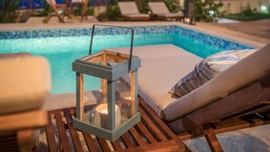 Un espace aménagé au bord de la piscine, avec des chaises longues, une table en bois surmontée d’une lanterne, et une vue sur la piscine.