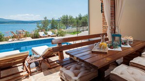 Une terrasse en bois avec une piscine, des chaises longues et une table sur laquelle se trouvent une bouteille et des verres.