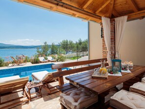 A wooden deck with a pool, lounge chairs, and a table with a bottle and glasses. - Vacation home  by Interhome (Pridraga)
