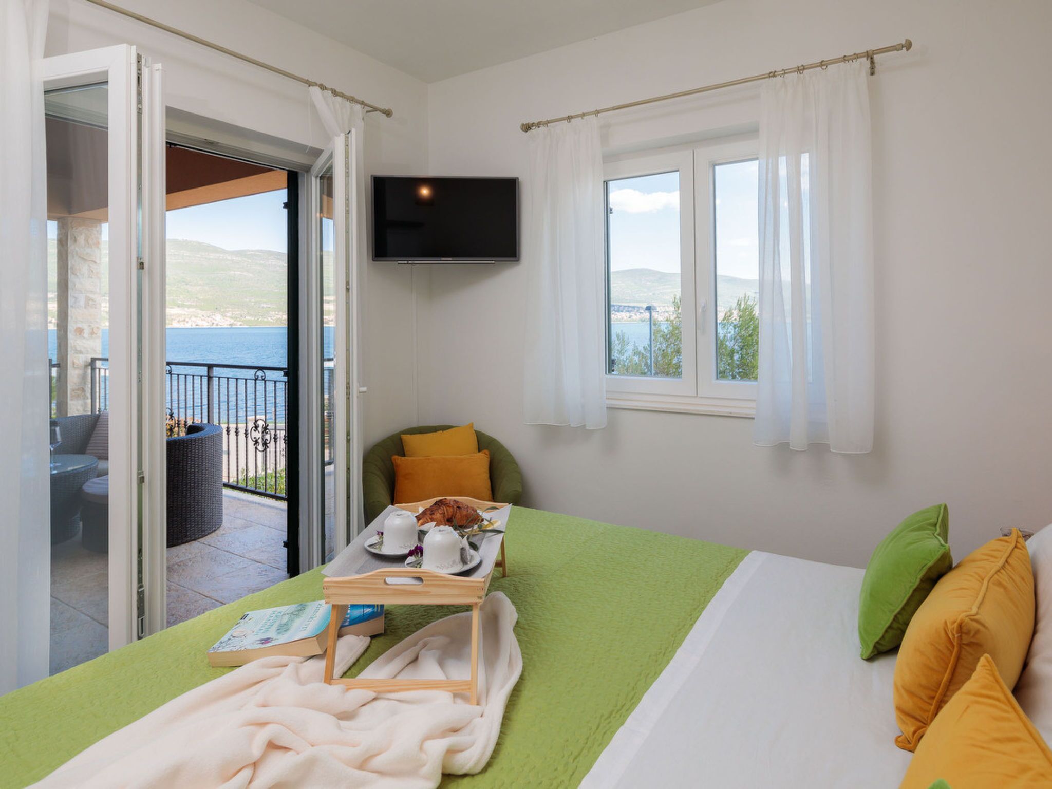 Een hotelkamer met een bed, een tafel met ontbijtartikelen, een televisie en een balkon met tuinmeubilair.