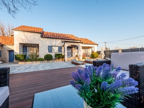 Ein modernes Haus mit Ziegeldach, einer überdachten Terrasse mit Gartenmöbeln und einem Garten voller lila Blumen.